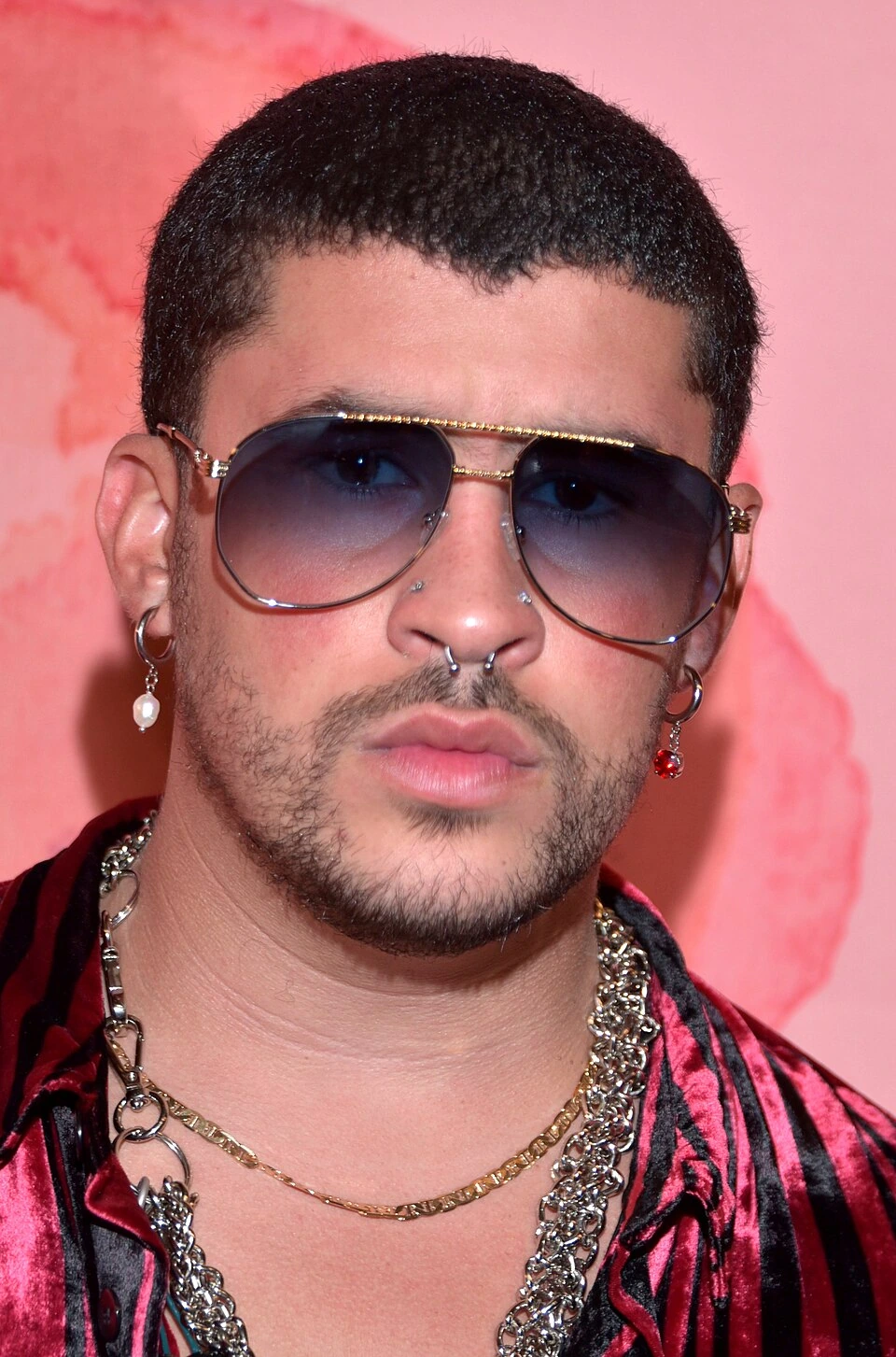 Bad Bunny portrait wearing sunglasses and jewelry against a pink background