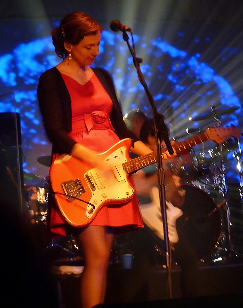 Bilinda Butcher performing on stage with an orange guitar under blue lighting